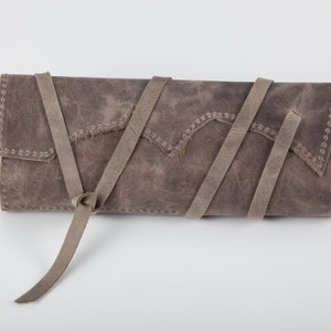 May include: A gray leather clutch with a long strap that can be tied in a knot. The clutch has a distressed look and is made of a soft, supple leather.