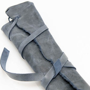 May include: A gray leather roll with a frayed edge, tied with blue leather straps.