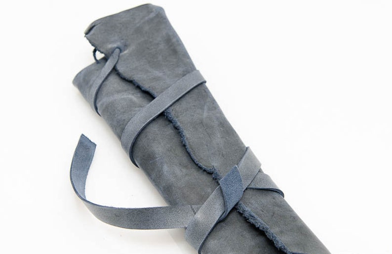 May include: A gray leather roll with a frayed edge, tied with blue leather straps.