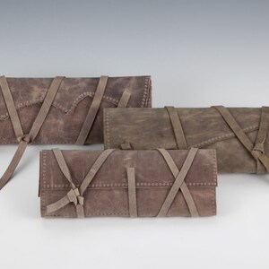 May include: Three brown leather pouches with straps and ties. The pouches are made of a distressed leather and have a rustic look.