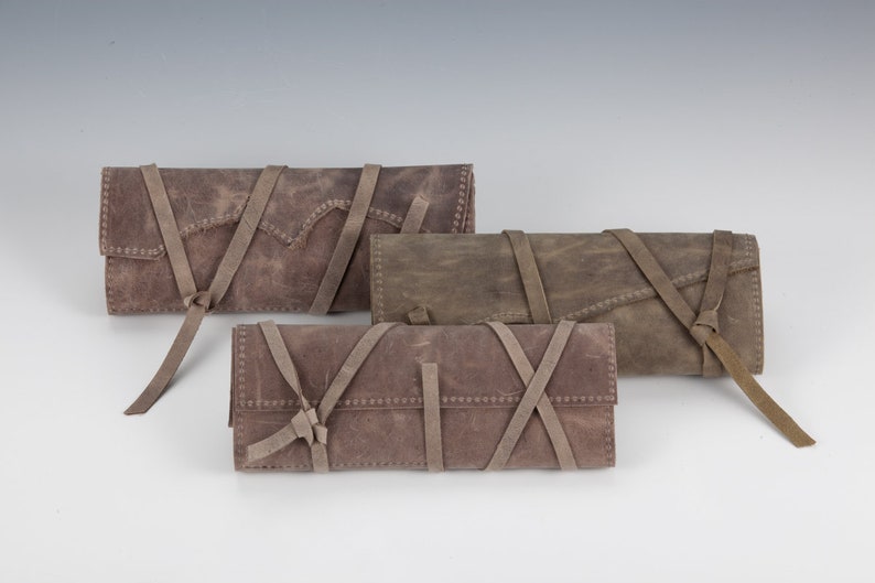 May include: Three brown leather pouches with straps and ties. The pouches are made of a distressed leather and have a rustic look.