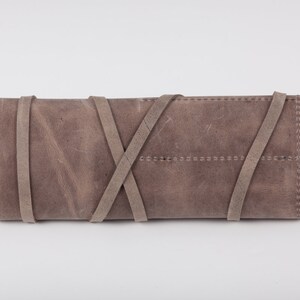 May include: A gray leather clutch with a braided strap closure.