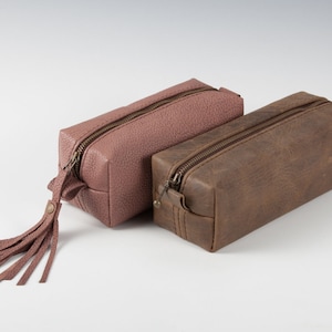 May include: Two leather zippered pouches, one brown and one dusty rose, with a tassel on the dusty rose pouch.