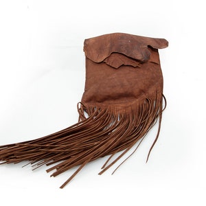 May include: A brown leather bag with a long fringe. The bag is made of a soft, supple leather and has a rustic, bohemian style.