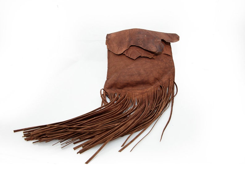 May include: A brown leather bag with a long fringe. The bag is made of a soft, supple leather and has a rustic, bohemian style.