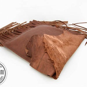 May include: A brown leather bag with fringe detailing. The bag is folded in half and the fringe is visible on both sides. The bag is made of a soft, supple leather and has a rustic, vintage look.