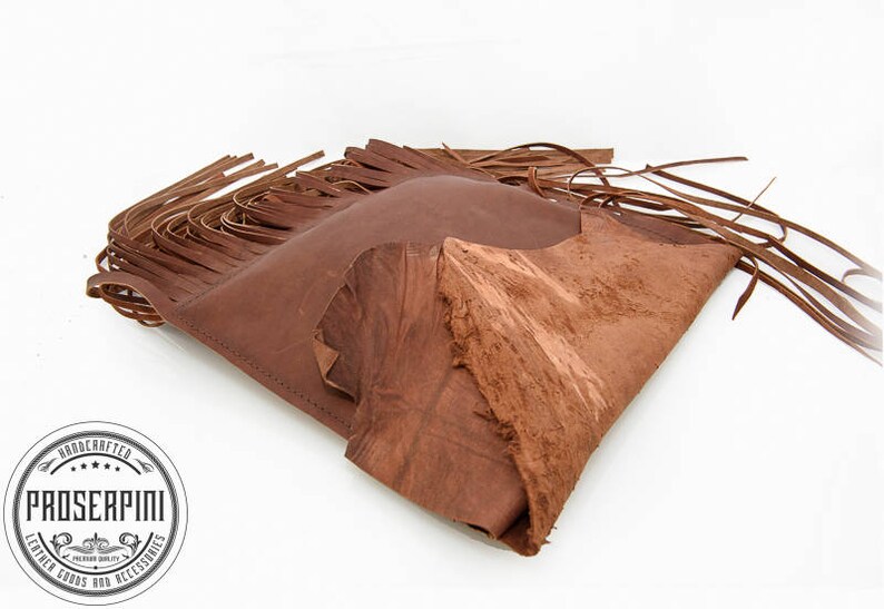 May include: A brown leather bag with fringe detailing. The bag is folded in half and the fringe is visible on both sides. The bag is made of a soft, supple leather and has a rustic, vintage look.