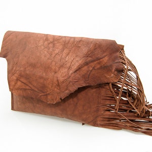 May include: A brown leather clutch with a fringe detail. The clutch has a textured surface and a flap closure.