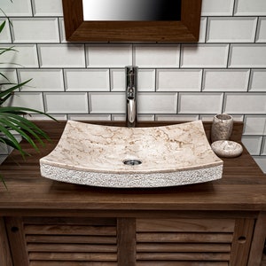 May include: A beige marble bathroom sink with a textured edge sits on a dark wood countertop. The sink is rectangular with rounded corners and has a single drain hole. A chrome faucet is mounted above the sink.