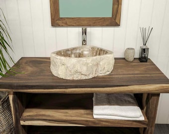 Könnte beinhalten: Ein Naturstein-Waschbecken mit rauer, strukturierter Außenseite und glattem Innenbecken, montiert auf einem dunklen Holzwaschtisch mit zwei offenen Regalen. Ein weißes, gefaltetes Handtuch liegt auf dem mittleren Regal, darüber ein Holzspiegel.