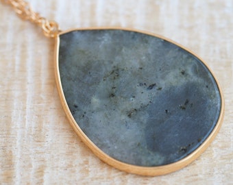 May include: A teardrop-shaped pendant necklace with a dark gray stone set in a gold-toned metal frame.