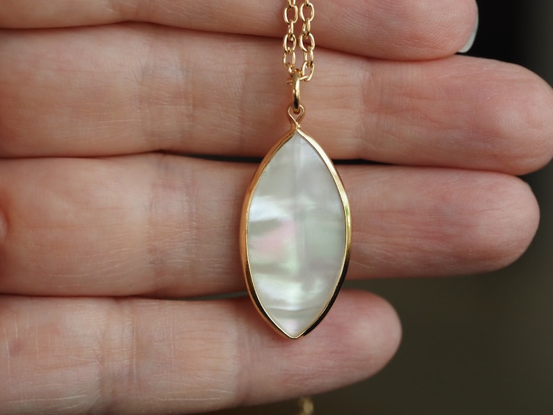 May include: A gold chain necklace with a white iridescent oval pendant. The pendant is set in a gold frame and has a subtle shimmer.