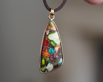 May include: A gold pendant necklace with a teardrop-shaped stone featuring a colorful, abstract pattern of green, blue, red, orange, and white.