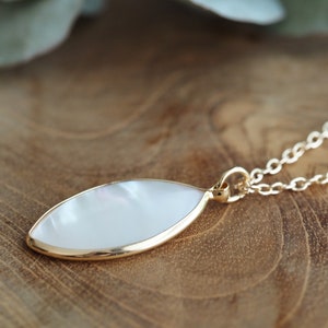 May include: A gold chain necklace with a white oval pendant. The pendant has a pearlescent finish and a gold rim.