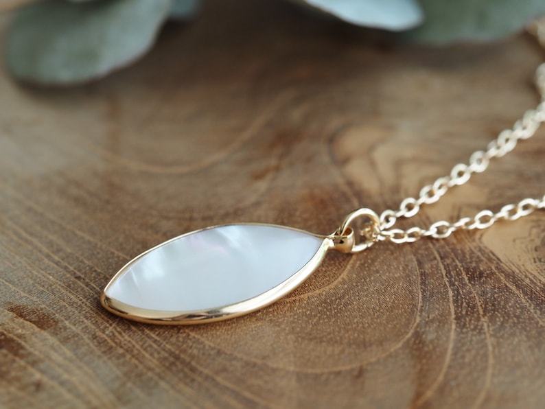 May include: A gold chain necklace with a white oval pendant. The pendant has a pearlescent finish and a gold rim.