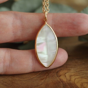 May include: A gold chain necklace with a white iridescent oval pendant. The pendant is shaped like a leaf and has a gold border.
