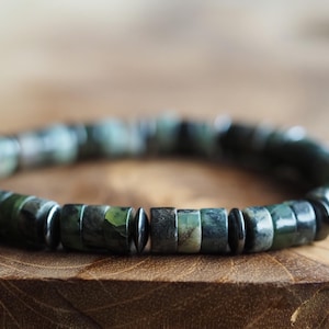 Op de afbeelding: Een armband gemaakt van donkergroene en zwarte kralen. De kralen zijn rond en hebben een gladde, gepolijste afwerking.