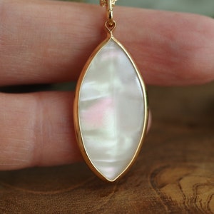 May include: A gold pendant necklace with a white iridescent oval-shaped stone.