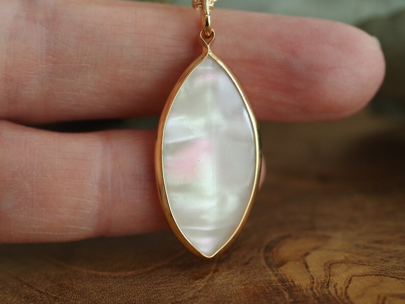 May include: A gold pendant necklace with a white iridescent oval-shaped stone.