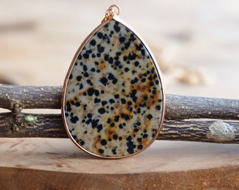 May include: A teardrop-shaped pendant necklace with a brown, black, and white speckled stone set in a rose gold frame.