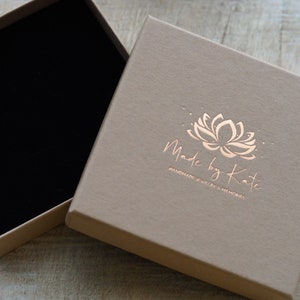 May include: A light brown square box with a black velvet interior. The box has a gold foil logo that says "Made by Kate" and "Handmade Jewelry & Memoires".