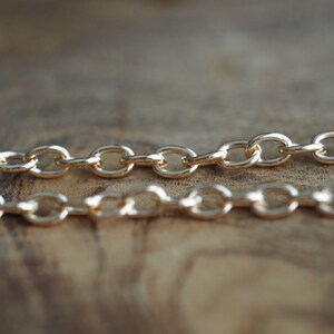 May include: Two gold chains with oval links, lying on a wooden surface.