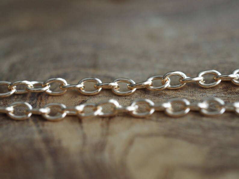 May include: Two gold chains with oval links, lying on a wooden surface.