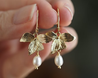 May include: Gold orchid flower earrings with a pearl dangle. The earrings are delicate and feminine.