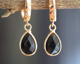 May include: A pair of gold hoop earrings with black teardrop-shaped stones. The stones have a faceted design.