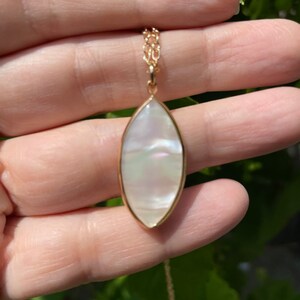 May include: A gold chain necklace with a white pearlescent oval pendant.