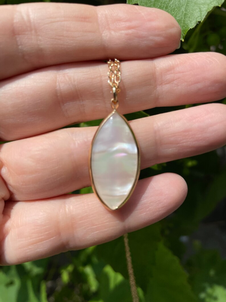 May include: A gold chain necklace with a white pearlescent oval pendant.