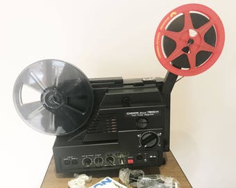 Op de afbeelding: Een zwarte Chinon 7800 H Two Track Magnetic Sound-filmprojector met een rode filmrol en een zwarte filmrol.