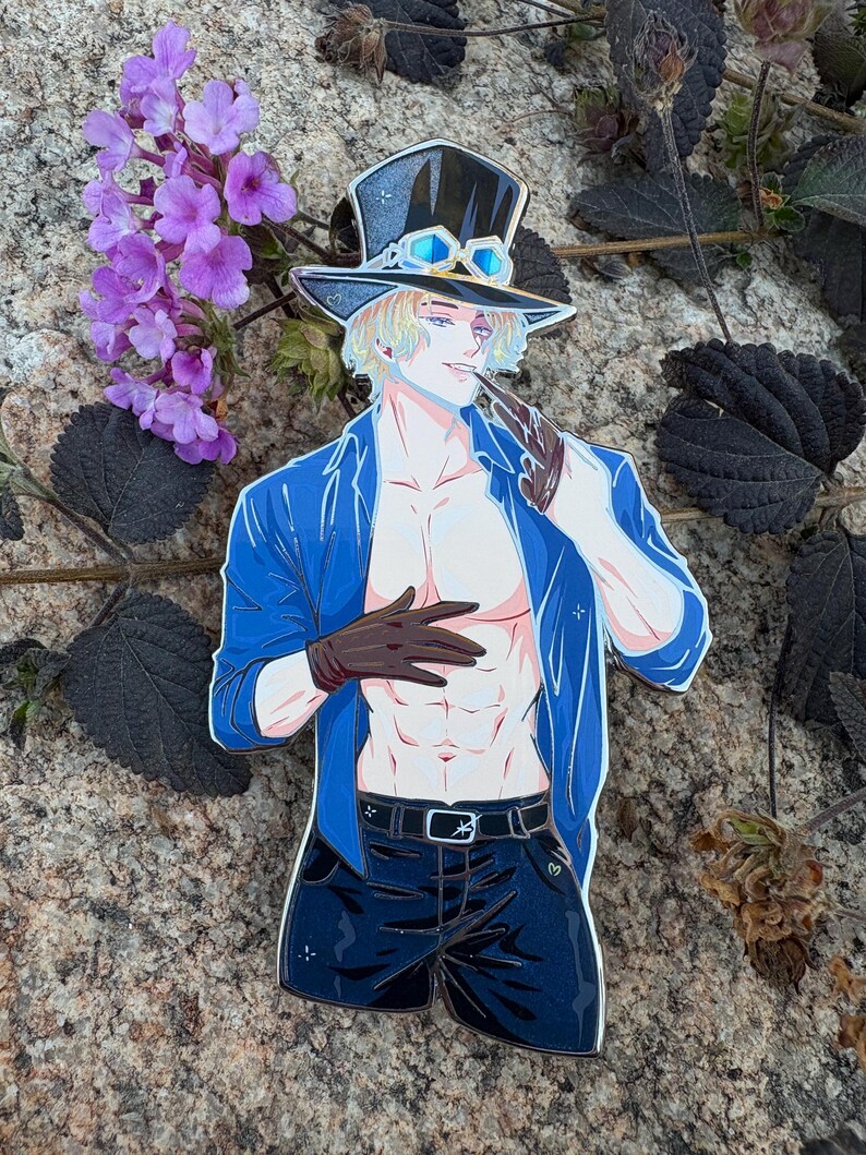 K&ouml;nnte beinhalten: Ein Anime-Pin mit einem Charakter mit blonden Haaren, der einen schwarzen Zylinder mit Brille, eine blaue Jacke, schwarze Shorts und braune Handschuhe tr&auml;gt. Die Figur h&auml;lt eine Pfeife. Der Pin befindet sich vor einem Naturstein-Hintergrund mit lila Blumen.