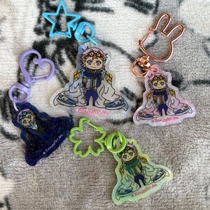 May include: A collection of colorful keychains featuring anime-style character designs. The keychains have various shapes, including a star, heart, flower, and bunny. Each keychain has a different color scheme and design, with the text "Remington Arts" on each.