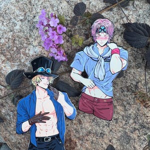 May include: Two anime-style character stickers. One sticker features a character in a blue jacket, black shorts, and a top hat with goggles. The other sticker depicts a character in a blue shirt and red shorts. Purple flowers and foliage are in the background.