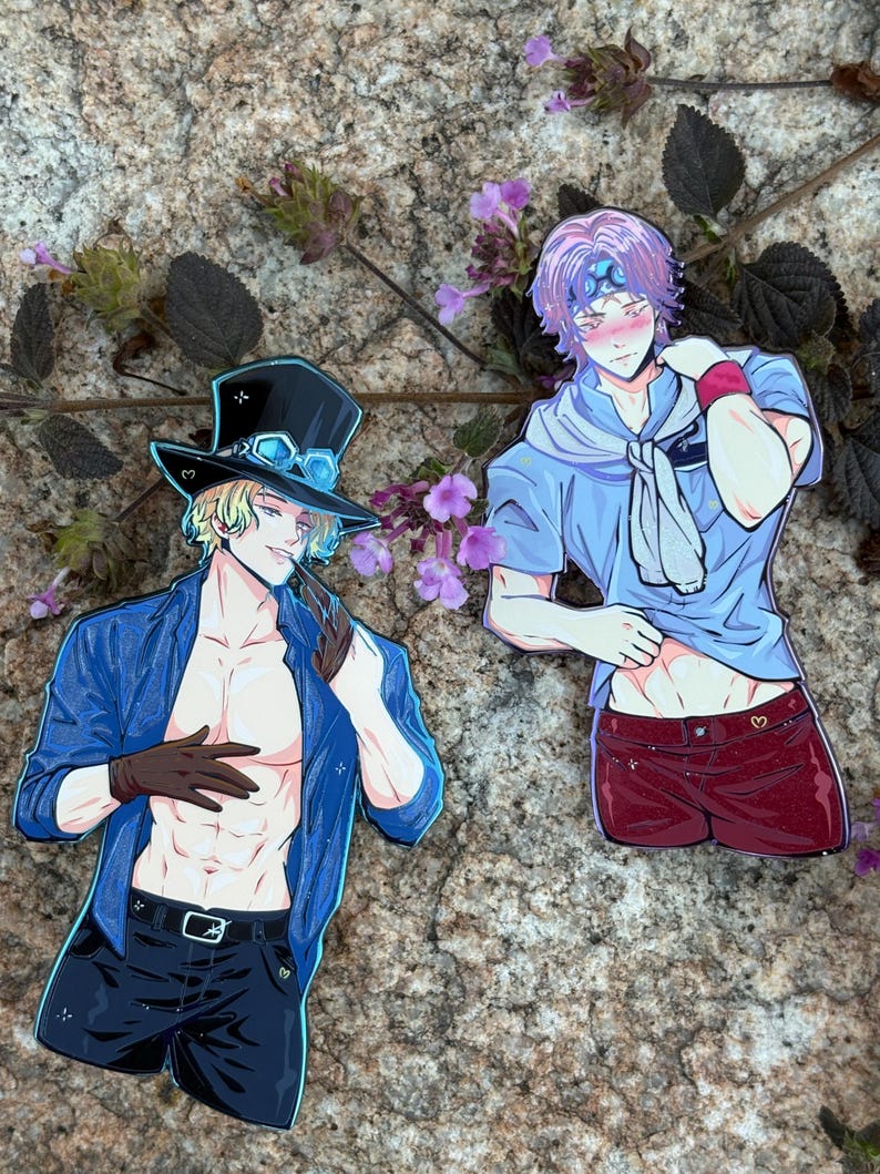 K&ouml;nnte beinhalten: Zwei Aufkleber mit Anime-Charakteren. Einer zeigt einen blonden Charakter in einer blauen Jacke, schwarzen Shorts und einem Zylinder. Der andere ist ein Charakter mit lila Haaren, einem blauen Hemd und roten Shorts. Beide sind auf einer Steinoberfl&auml;che abgebildet.