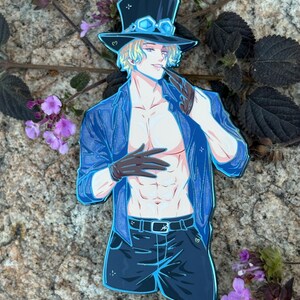 K&ouml;nnte beinhalten: Ein gestanzter Aufkleber mit einer Figur mit blonden Haaren, die einen blauen Zylinder mit Brille, eine blaue Jacke, schwarze Handschuhe und schwarze Shorts tr&auml;gt. Die Figur h&auml;lt eine Pfeife. Der Aufkleber befindet sich auf einer Steinoberfl&auml;che mit lila Blumen.