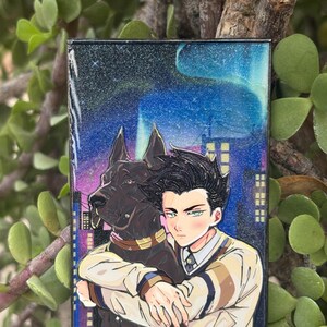 May include: A rectangular enamel pin featuring a black dog and a person with dark hair wearing a beige sweater, set against a glittery night sky with a blue aurora and city buildings. The pin has a black nickel finish and includes the text Black Nickel.