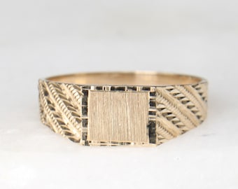 May include: A gold signet ring with a textured band and a blank square top.