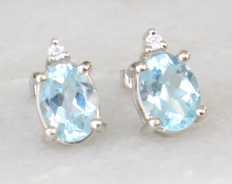 May include: A pair of silver earrings with oval-shaped blue topaz gemstones and small clear diamonds.
