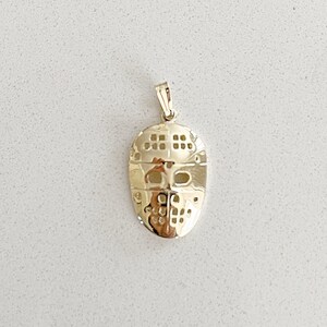 K&ouml;nnte beinhalten: Ein goldfarbener Anh&auml;nger in Form einer Hockeymaske. Die Maske hat ein detailliertes Design mit einem Netz-Muster und Augenl&ouml;chern.
