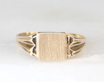 May include: A gold signet ring with a brushed finish on the square top.