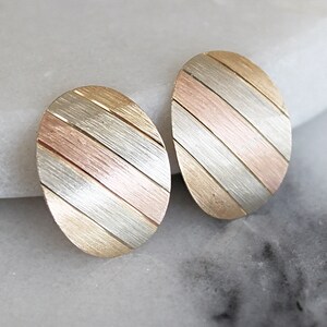 May include: A pair of oval-shaped earrings with a striped design in gold, silver, and rose gold.