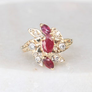 May include: A gold ring featuring three red ruby stones and small clear diamonds set in a leaf design.