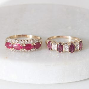Peut inclure: Deux bagues en or ornées de rubis et de diamants. La bague de gauche présente des rubis ovales et de petits diamants. La bague de droite alterne rubis ovales et diamants carrés. Les deux bagues sont posées sur une surface blanche.
