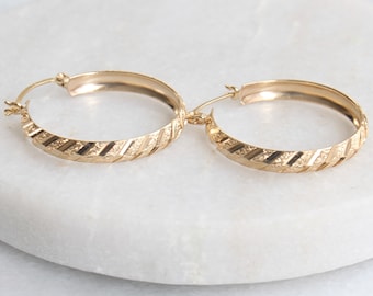 May include: A pair of gold hoop earrings with a textured, diagonal pattern. The earrings are simple and elegant.