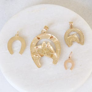 May include: Four gold-colored horseshoe pendants. Two of the pendants are simple horseshoes, while the other two feature a horse's head design.