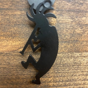 May include: Black metal Kokopelli figurine ornament. The figurine is playing a flute and has a distinctive headdress.