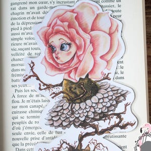 Può includere: Un adesivo stravagante con un personaggio con la faccia di rosa con una testa di rosa rosa, occhi blu e una gonna dettagliata e a strati. L'adesivo è ambientato su uno sfondo di pagine di libro.