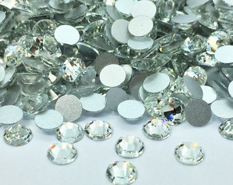 Puede incluir: Un montón de piedras de cristal transparentes con respaldo plateado. Las piedras están esparcidas sobre una superficie blanca.